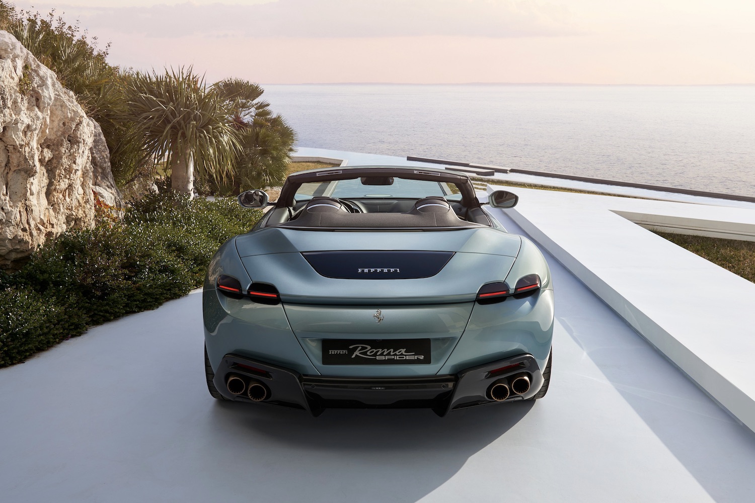 Close up of rear end of the 2024 Ferrari Roma parked in a driveway with the ocean in the back.