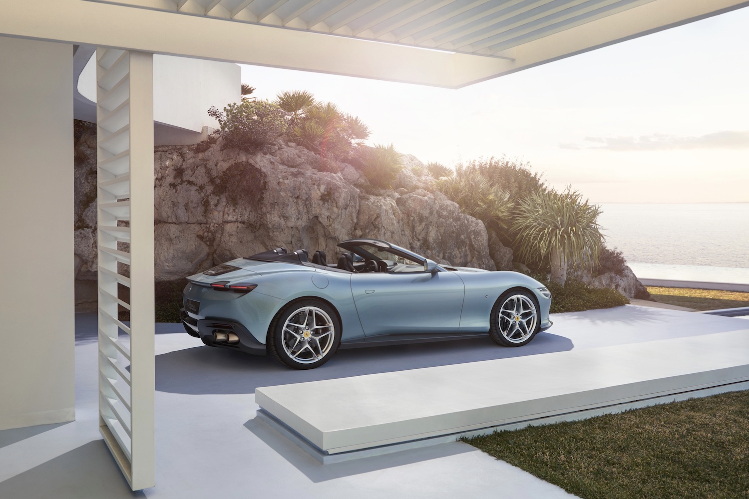 Rear end side profile of the 2024 Ferrari Roma from the passenger's side in front of jagged rocks.