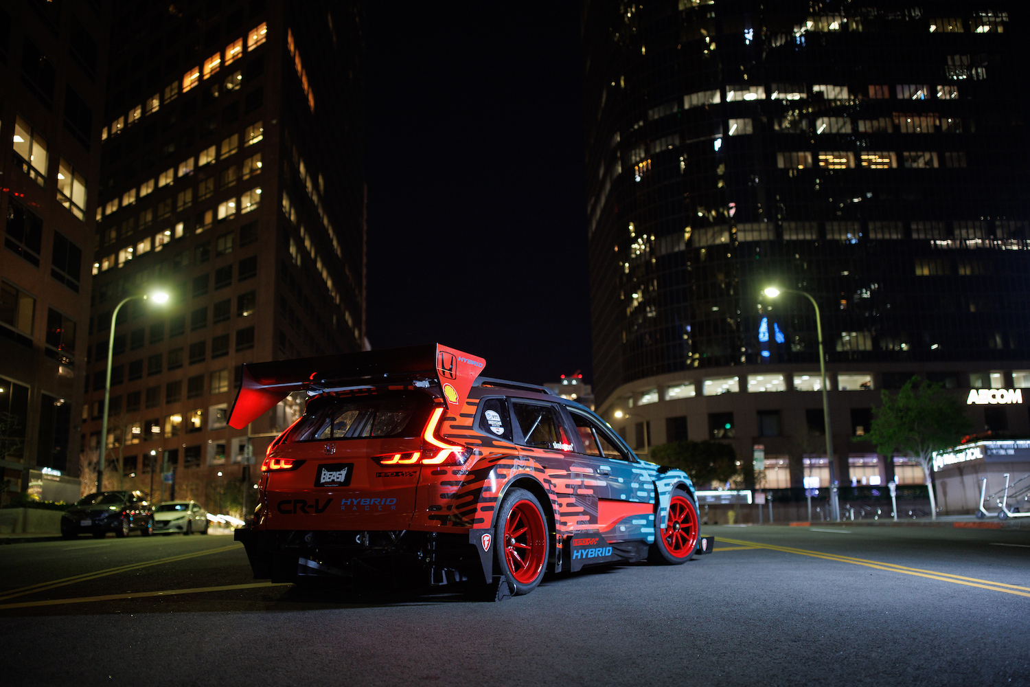 Rear end angle of the Honda CR-V Hybrid Racer parked in the middle of the road in front of tall buildings.