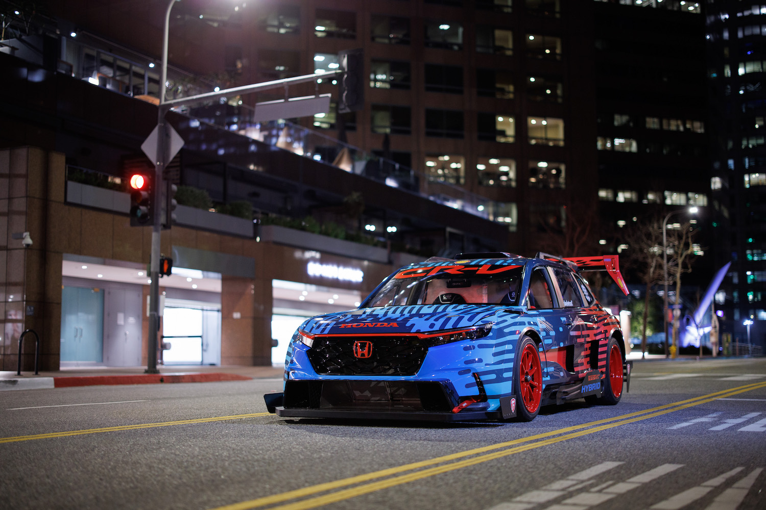Front end angle of the Honda CR-V Hybrid Racer parked in the middle of the street at night in front of tall buildings.