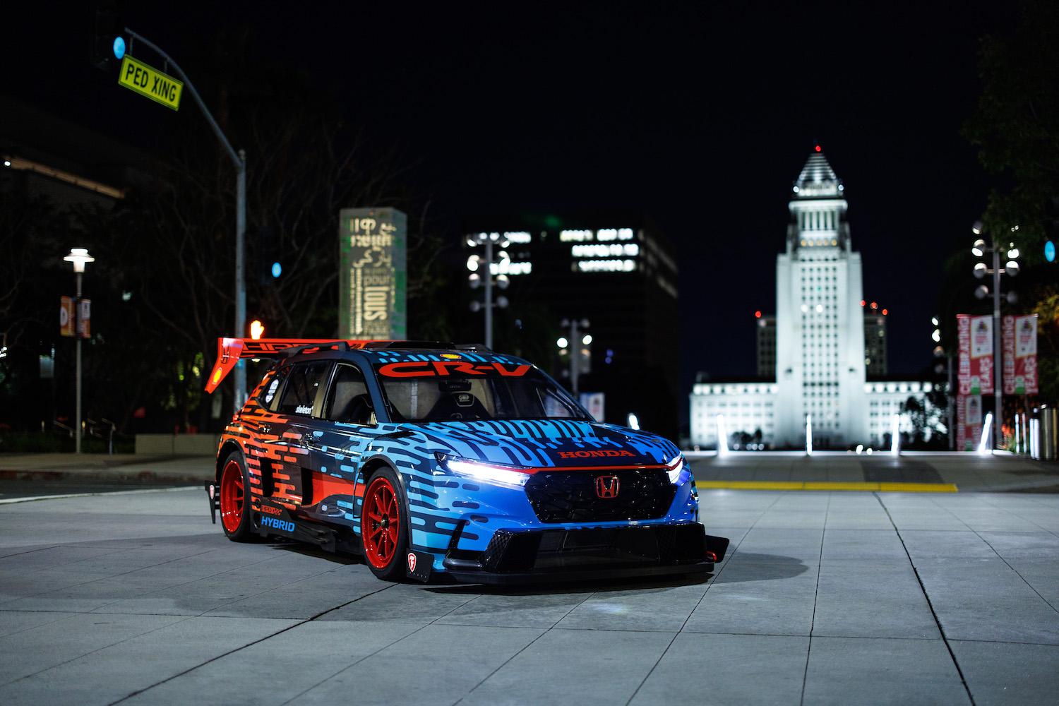 Front end angle of the Honda CR-V Hybrid Racer from the passenger's side at night in front of a statute.