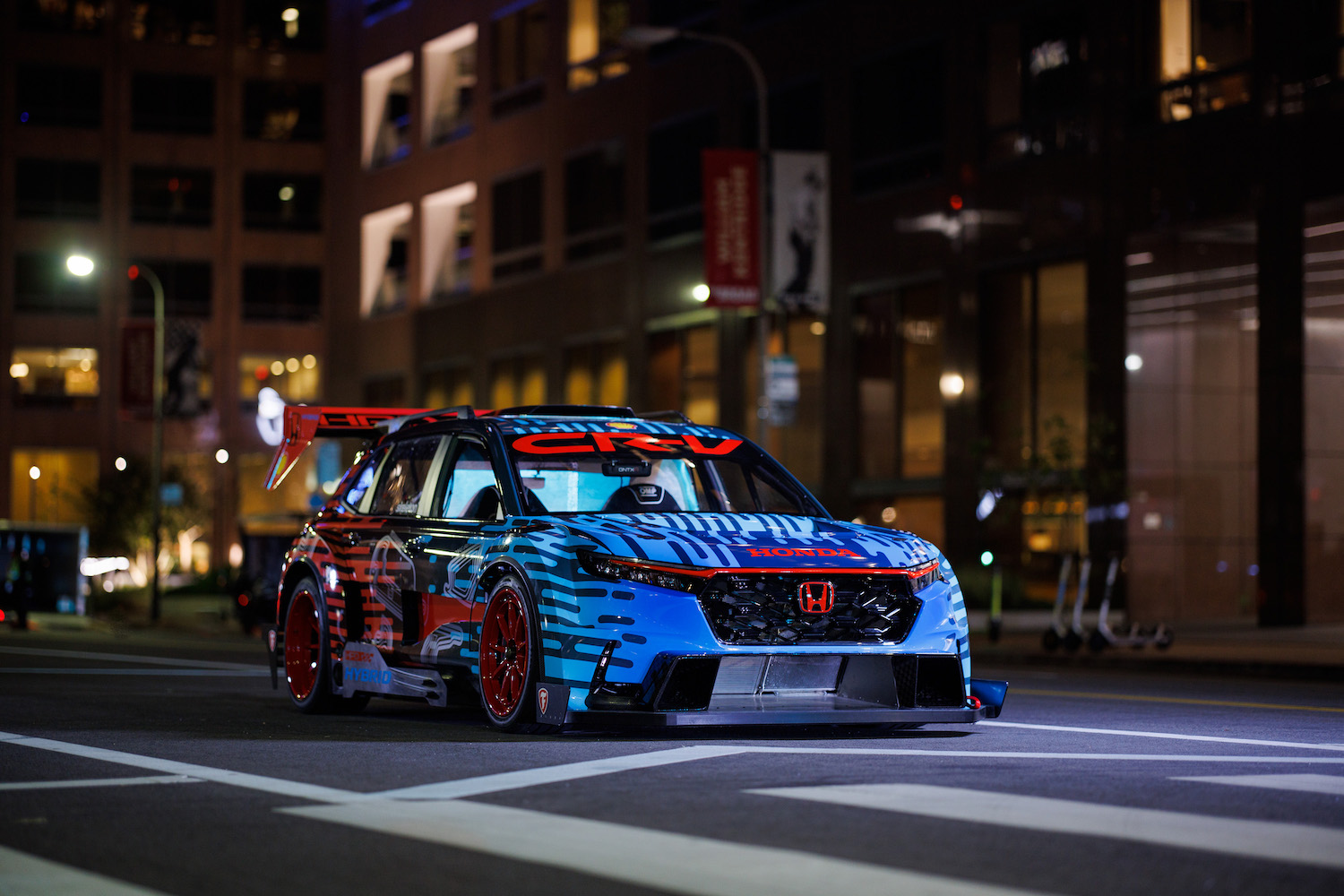 Close up of front end of the Honda CR-V Hybrid Racer parked in the middle of the road at night in front of buildings.