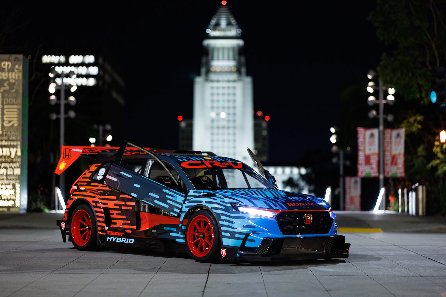 Front end angle of the Honda CR-V Hybrid Racer from the passenger's side parked in front of a statute at night.