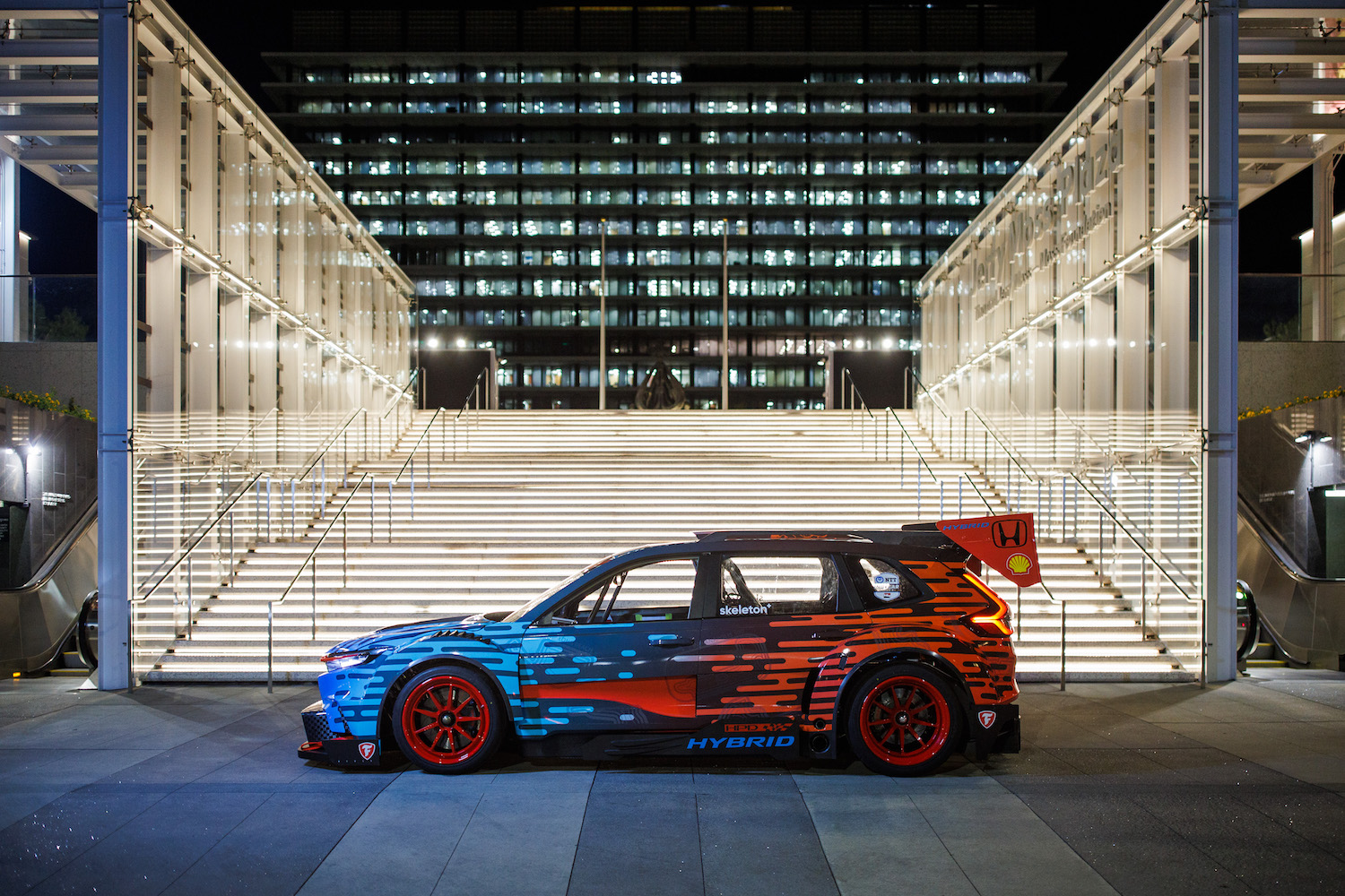 Side profile of the Honda CR-V Hybrid Racer parked in front of white stairs at night.