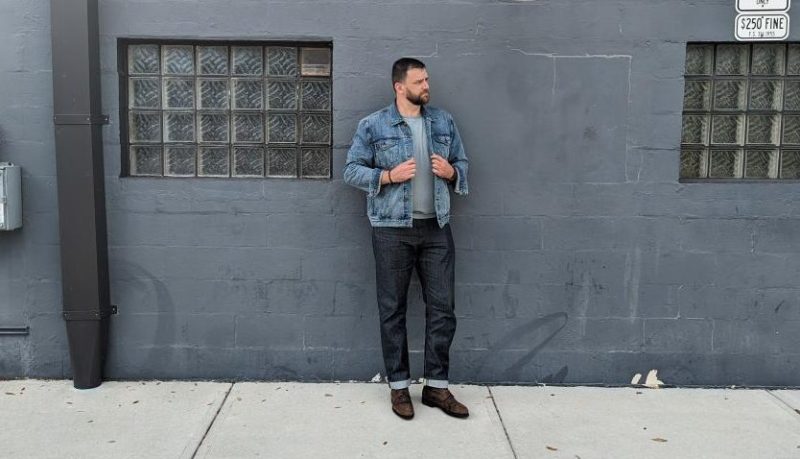 Man leaning on wall in denim jeans and jacket