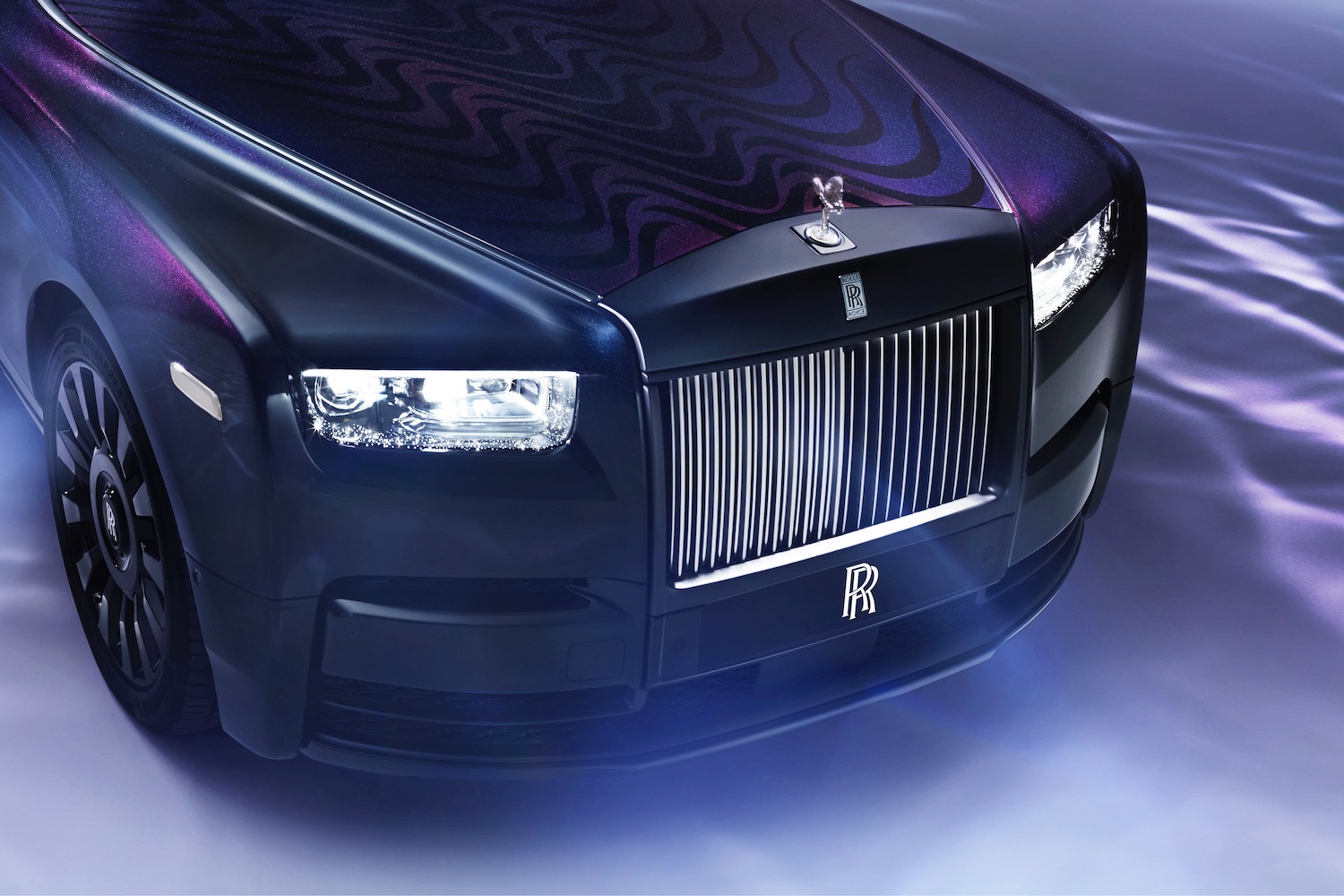 Close up of front end of the Rolls-Royce Phantom Syntopia from overhead with lights on and smoke in front of the car.