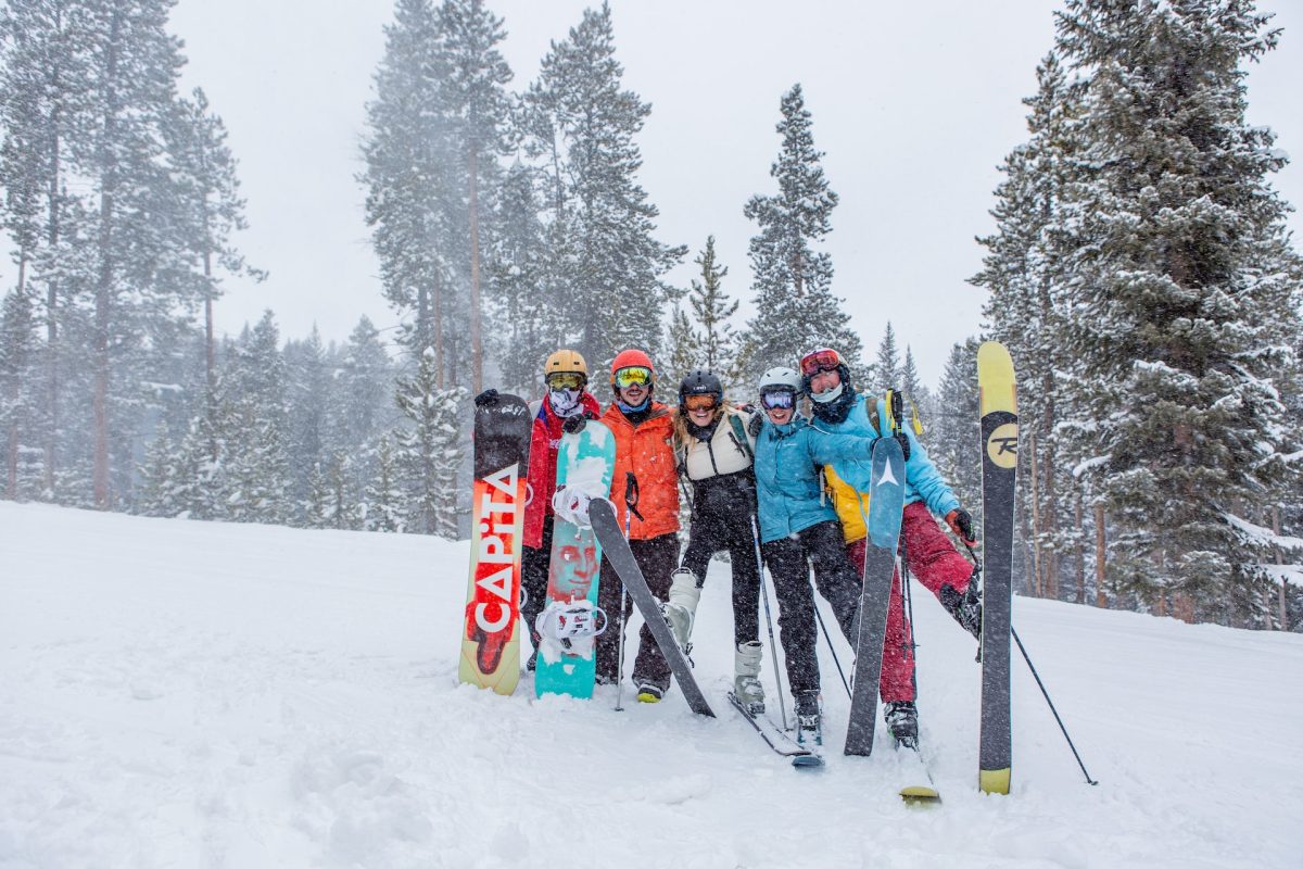 A group of friends posing with their snowboards and skis while standing in the snow.