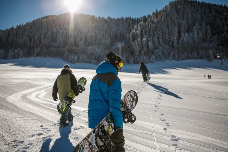 People carrying their snow gear through the snow.