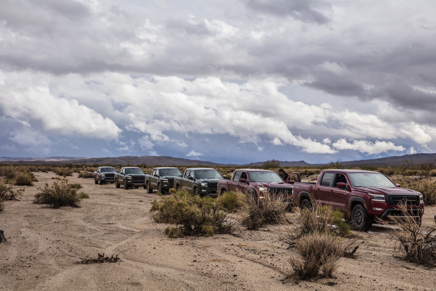 Side profile of the 2022 Nissan Frontier Pro-4X parked in a line on a dirt trail with storm clouds in the back.