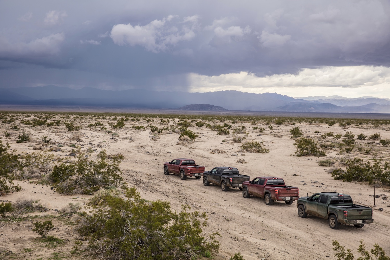 Rear end of 2022 Nissan Frontier Pro-4X parked in a line on a dirt trail with storm clouds in the back.