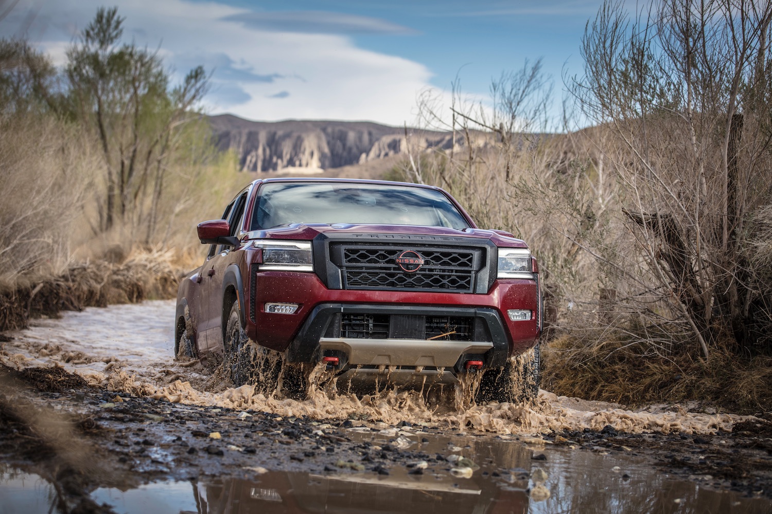 Close up of 2022 Nissan Frontier Pro-4X emerging from fording through water in the desert.