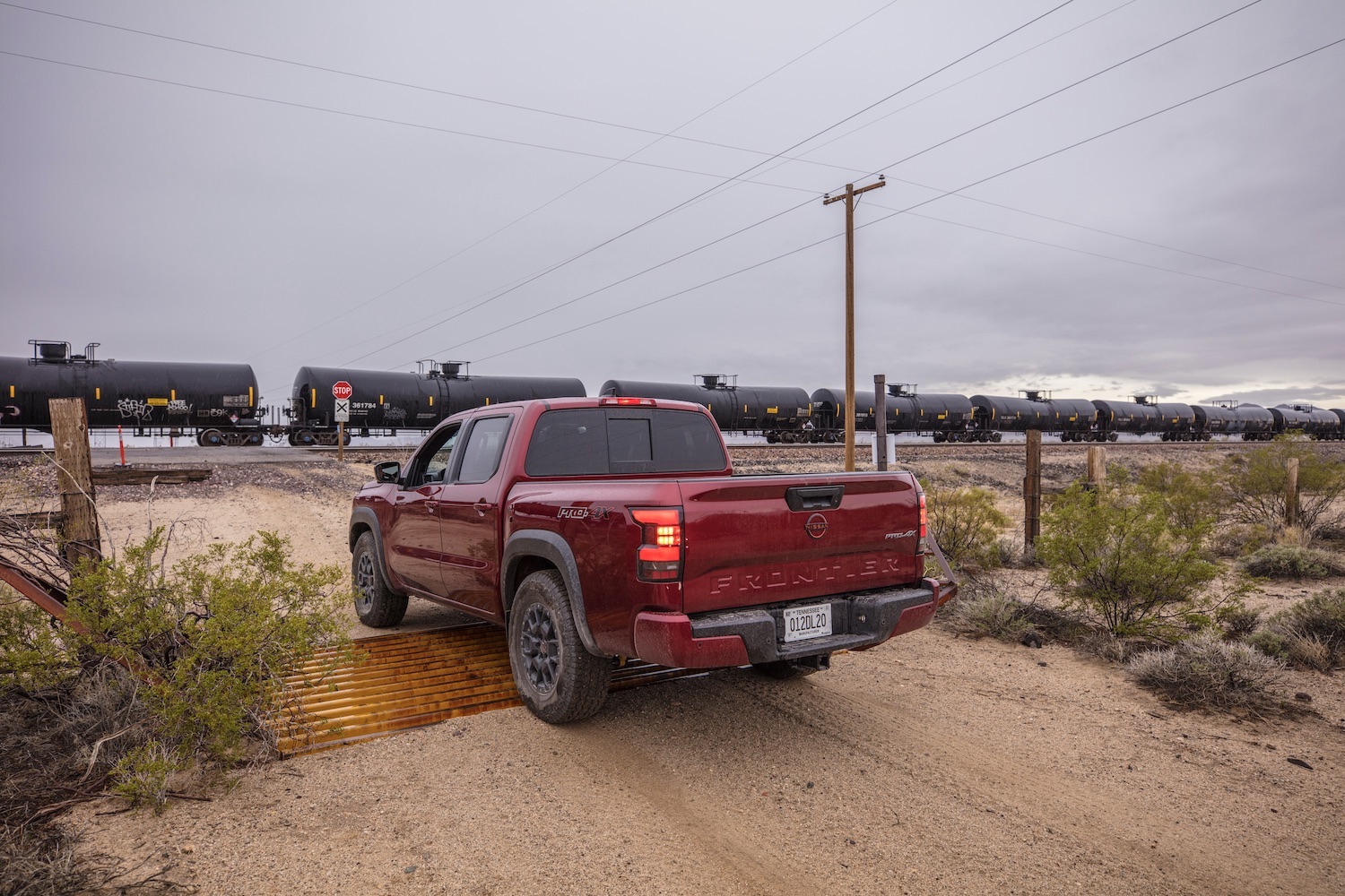 Rear end angle of the 2022 Nissan Frontier Pro-4X on a dirt trail with a train passing in the back.