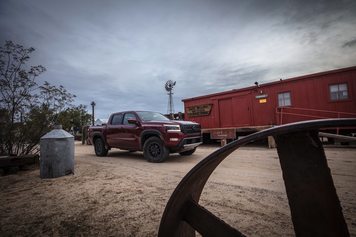 Front end angle of the 2022 Nissan Frontier Pro-4X parked in front of a red building on a dirt trail.