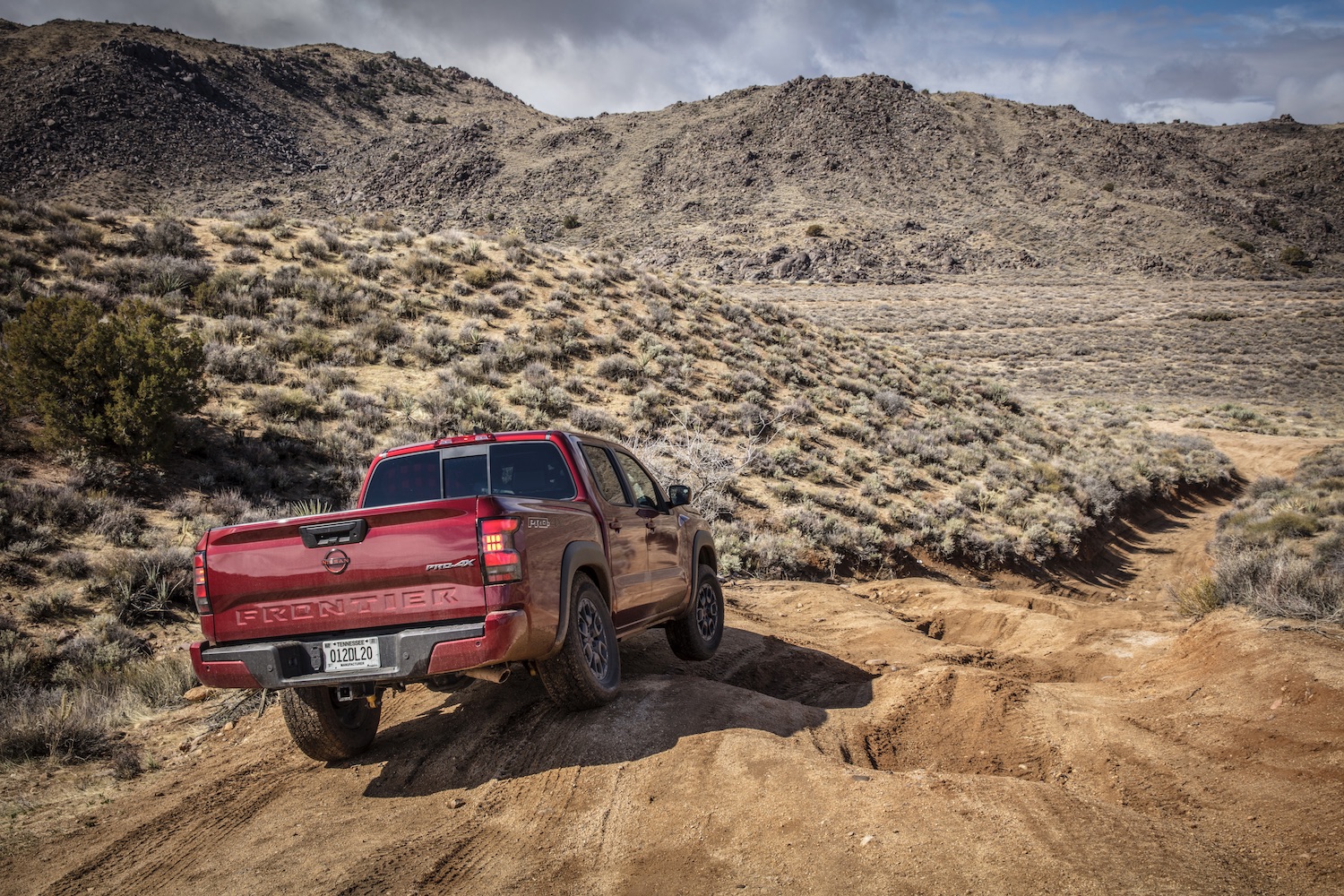 2022 Nissan Frontier Pro-4X rear end off-roading down a steep hill with mountains in the back.