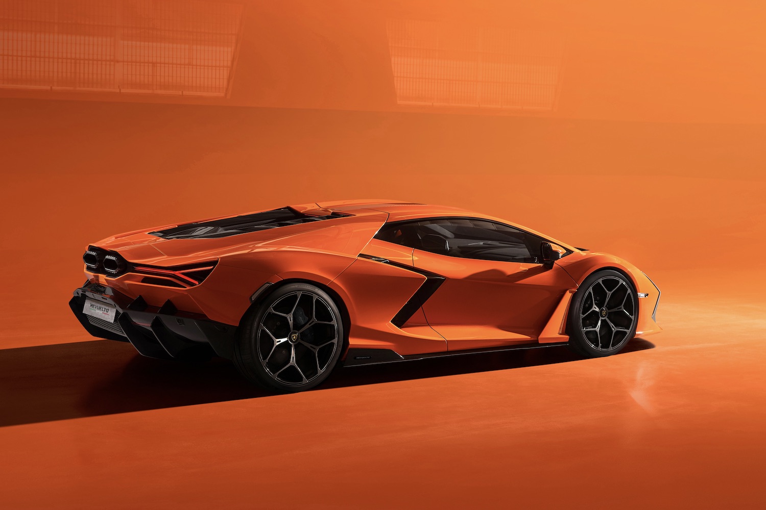 Rear end angle of the 2024 Lamborghini Revuelto from passenger's side with an orange background.