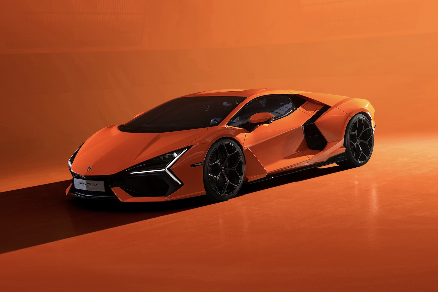 Front end angle of the 2024 Lamborghini Revuelto from driver's side in front of an orange background.