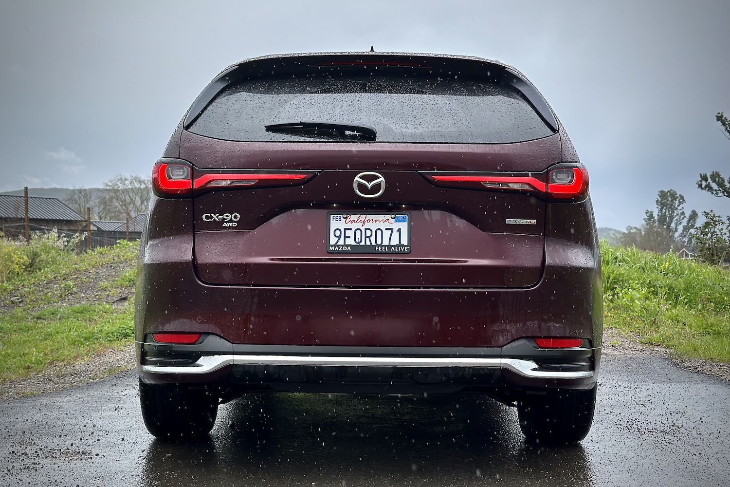 Close up of rear end of the 2024 Mazda CX-90 parked in front of green grass.