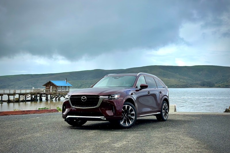 2024 Mazda CX-90 front end angle parked in front of a mountain and lake.
