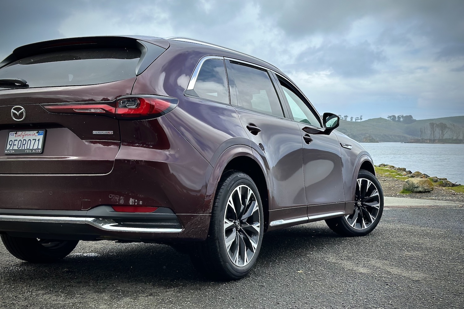 Rear end silhouette of the 2024 Mazda CX-90 from the passenger's side in front of a lake.