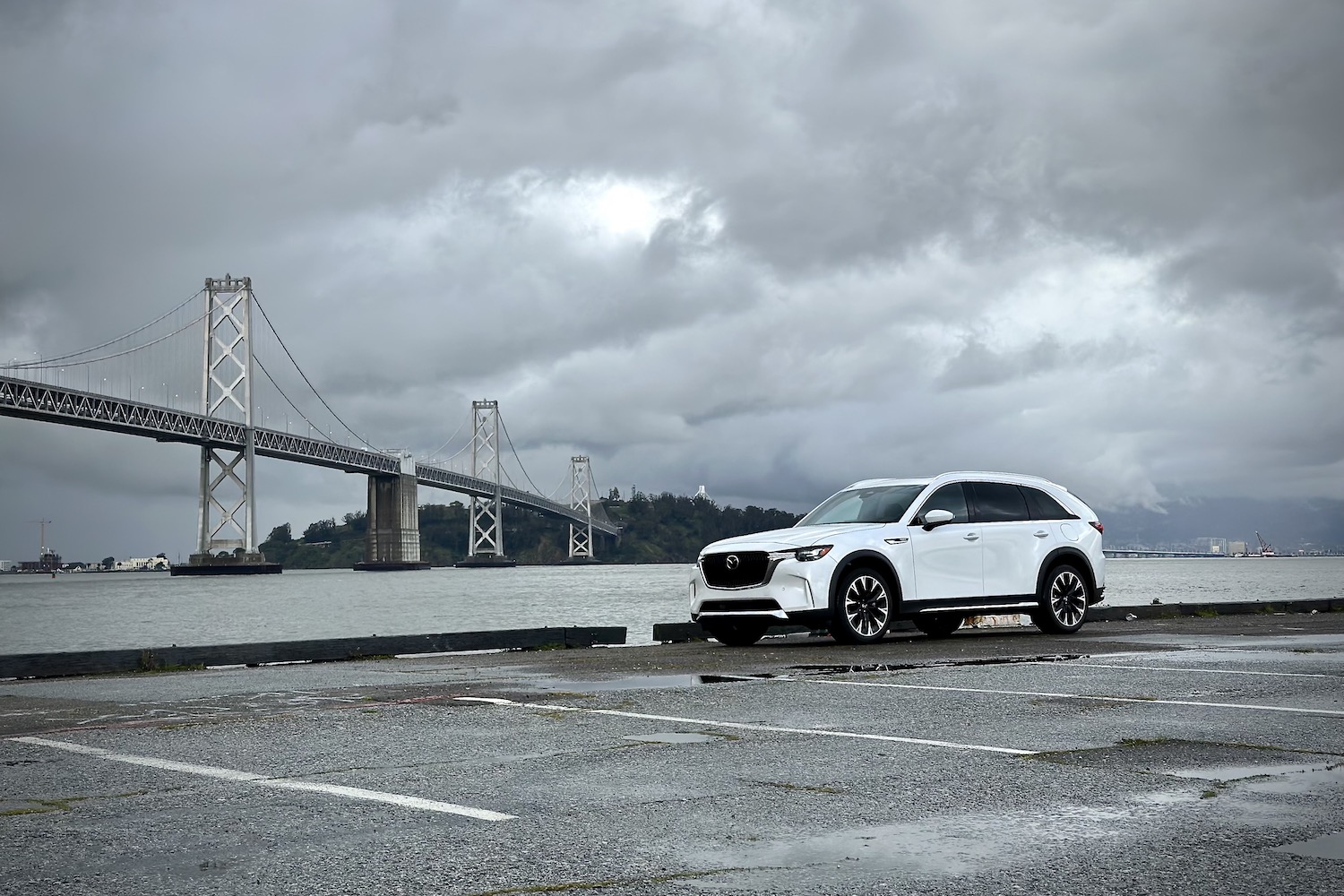 Side profile of the 2024 Mazda CX-90 PHEV parked in front of a bridge with dark clouds.