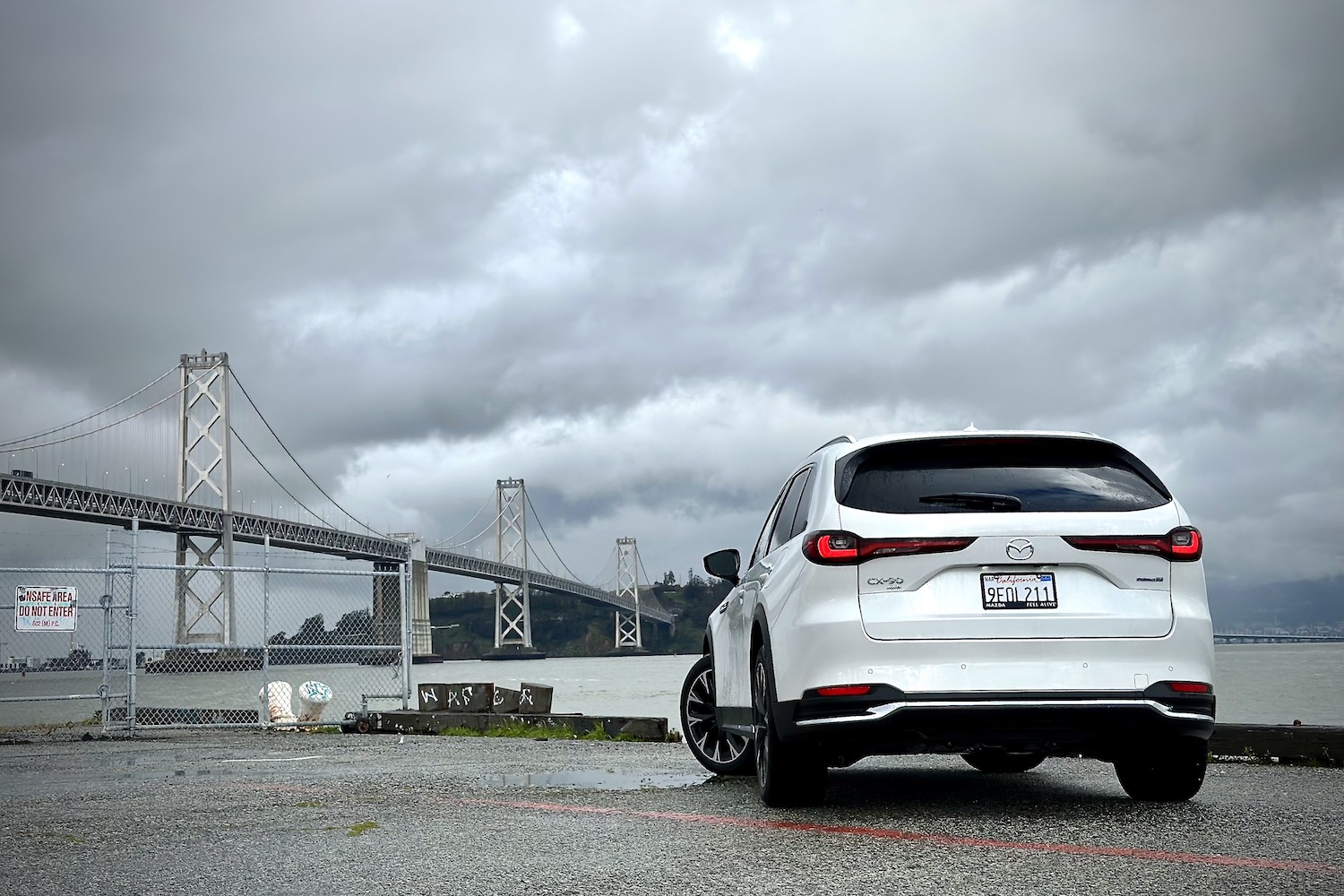 Close up of rear end of the 2024 Mazda CX-90 PHEV in front of a bridge and dark clouds.