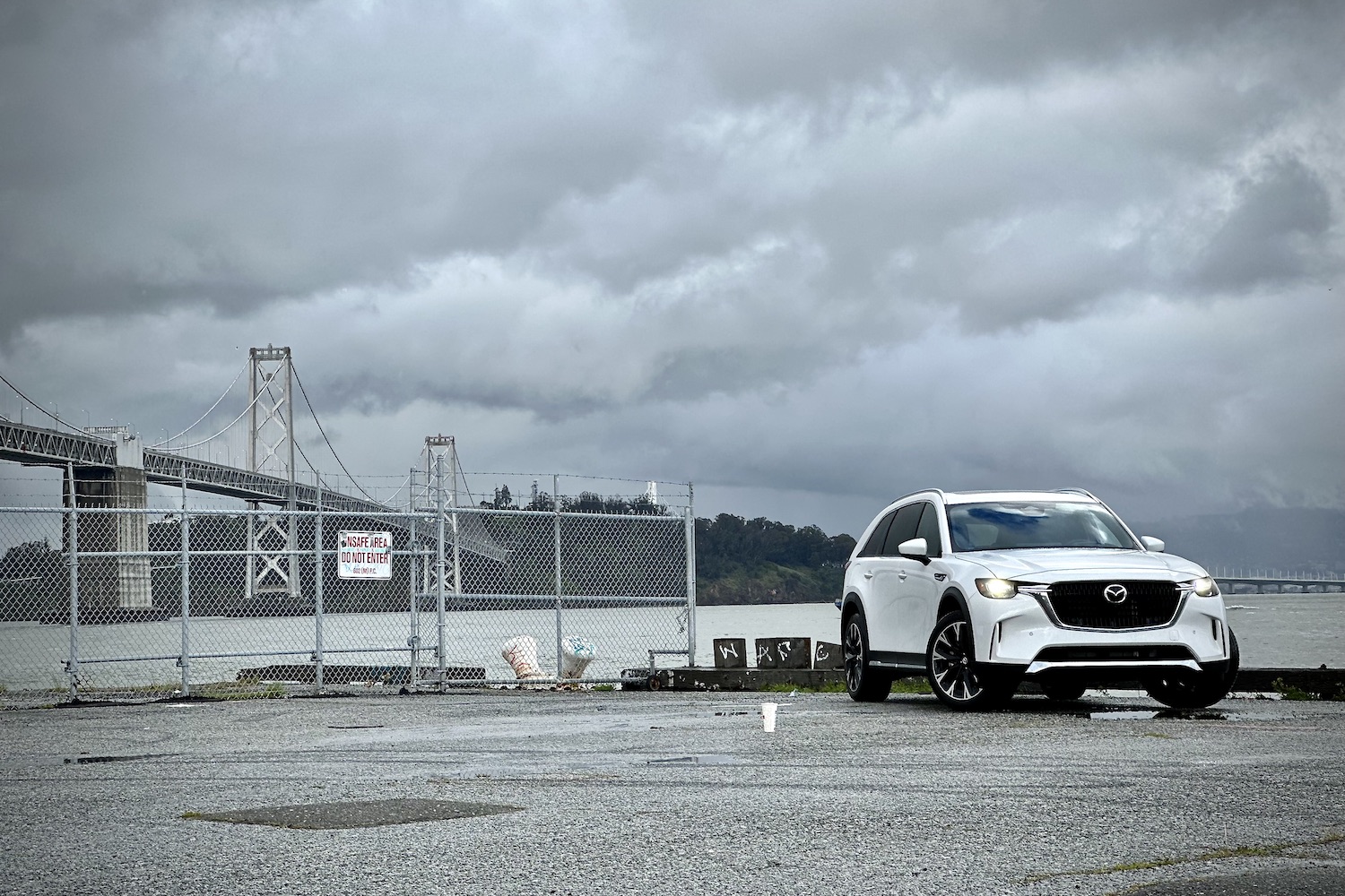 Front end angle of the 2024 Mazda CX-90 PHEV parked in front of a bridge and dark clouds.