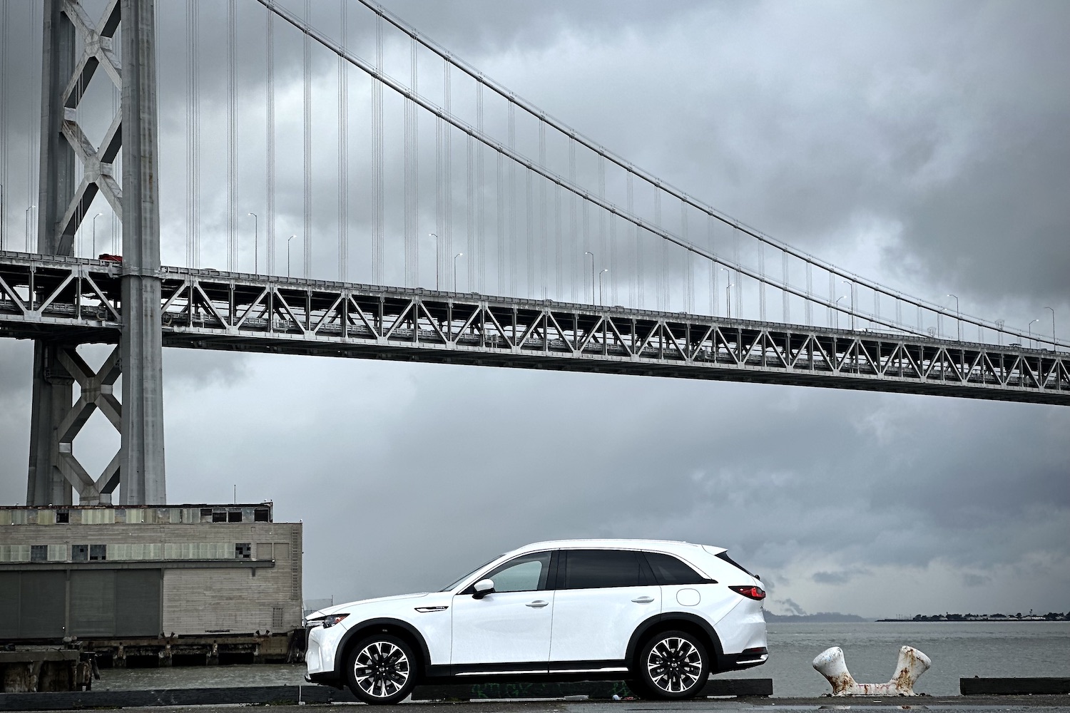 Side profile of the 2024 Mazda CX-90 PHEV parked in front of a bridge.