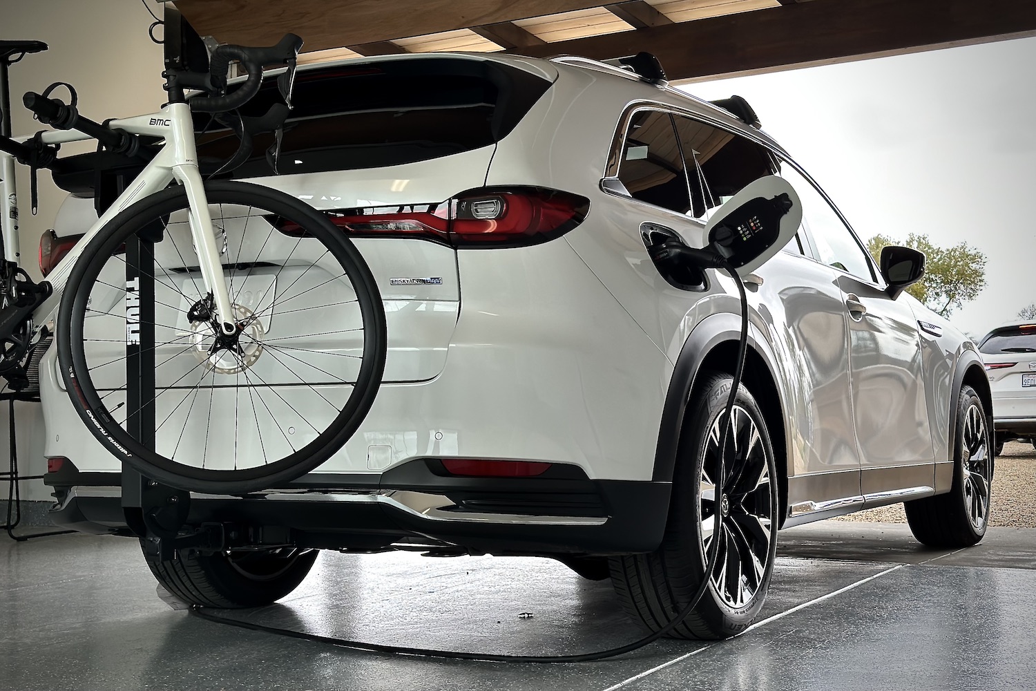 Rear end angle of the 2024 Mazda CX-90 PHEV parked in a garage when plugged into a charger.