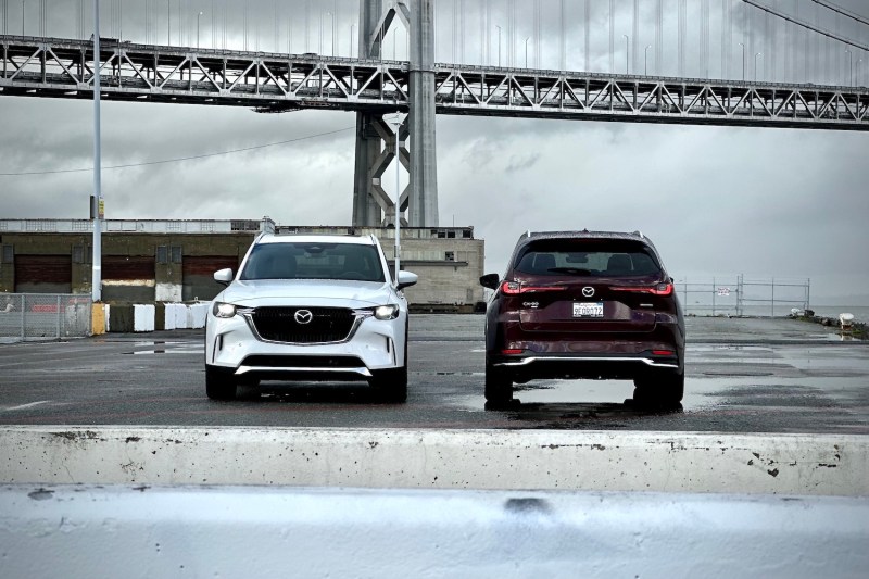 2024 Mazda CX-90 and PHEV parked in front of a large bridge.