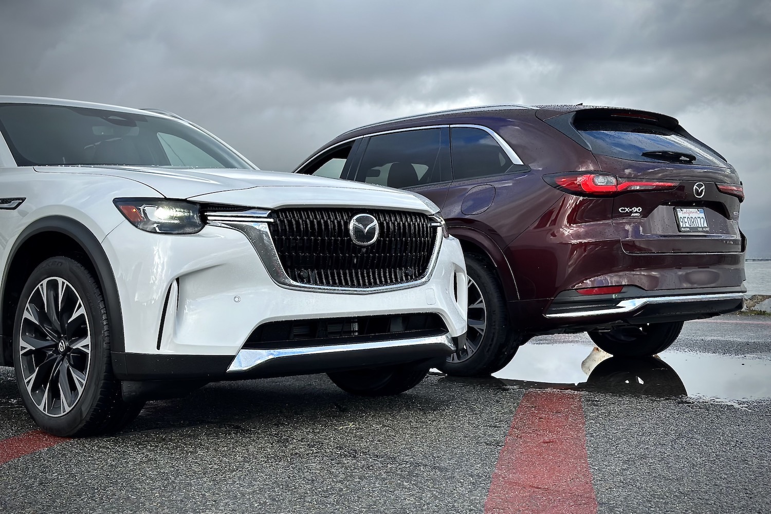 Front and rear end of the 2024 Mazda CX-90 and PHEV parked in front of dark clouds.