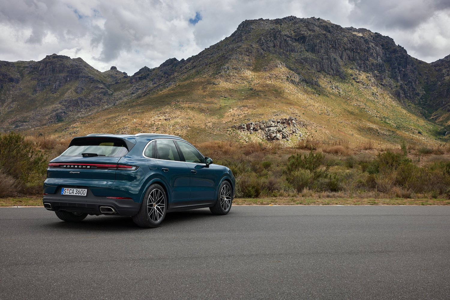 Rear end angle of the 2024 Porsche Cayenne from passenger's side parked in front of mountains.