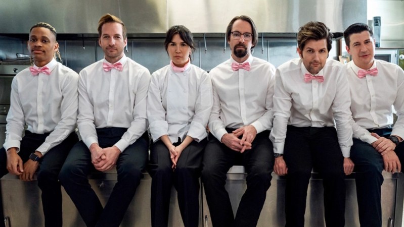 The cast of Party Down in uniform sitting on a counter.