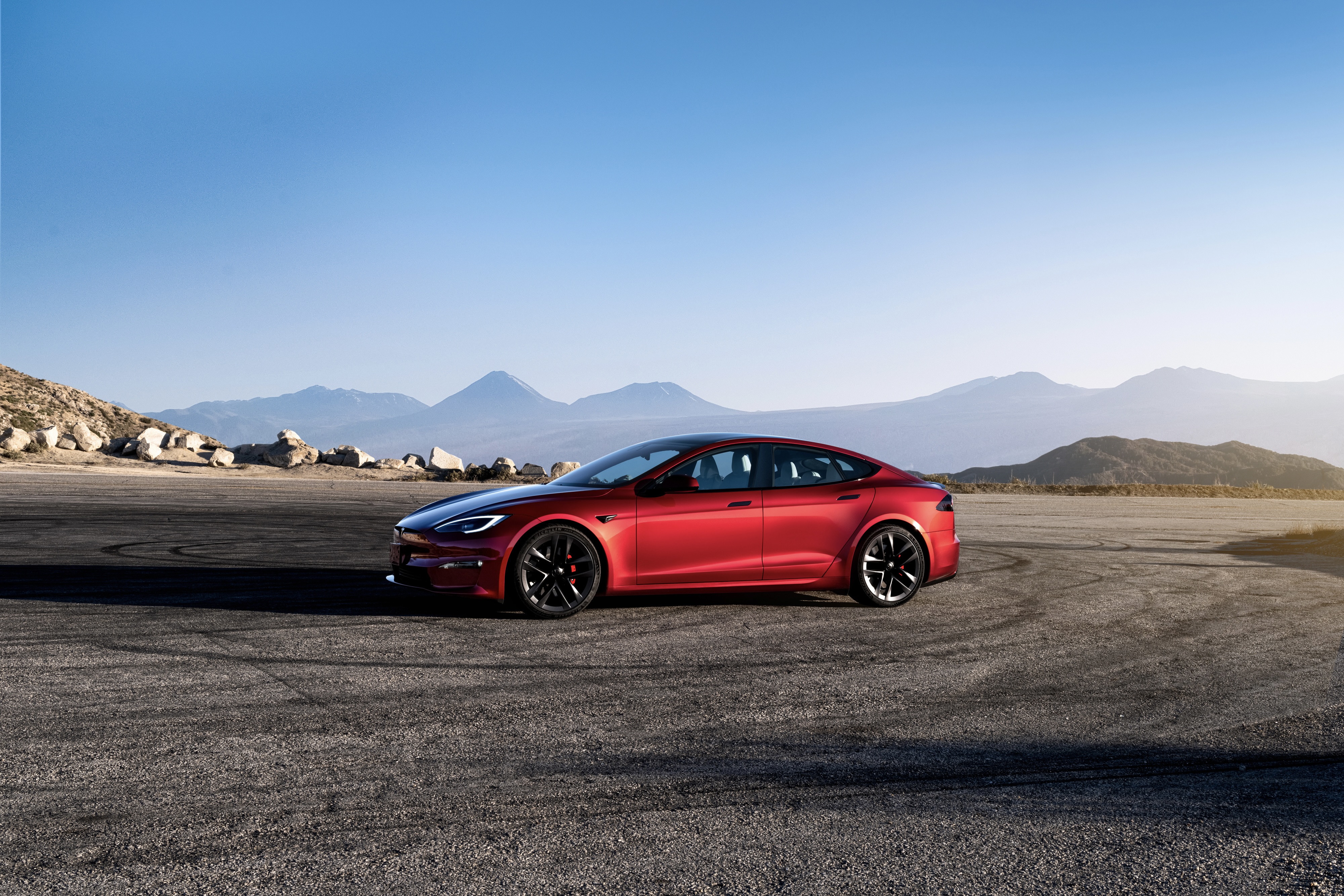 Tesla Model S side profile from front end parked in front of mountains with a blue sky.