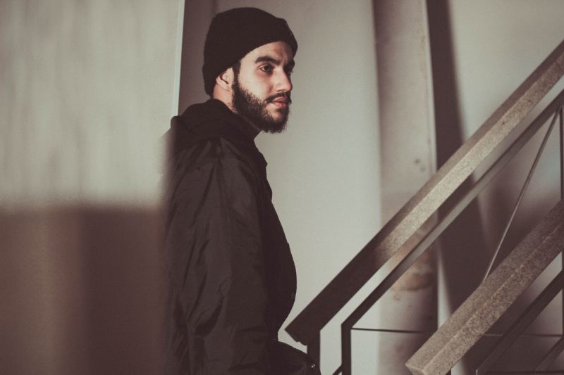 Bearded young man with a skull cap on walking up stairs.