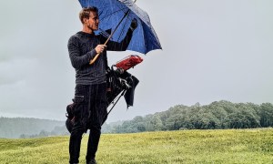 man on golf course in rain storm with umbrella