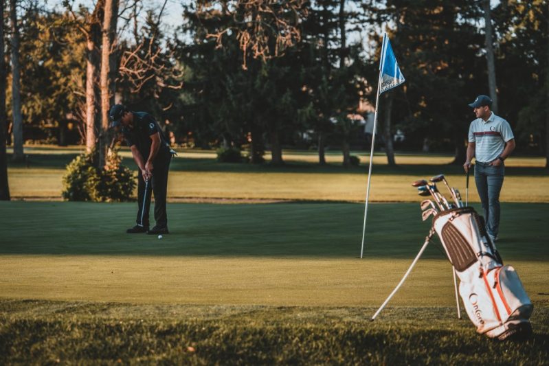 People on the golf course with a golf bag standing on the side.