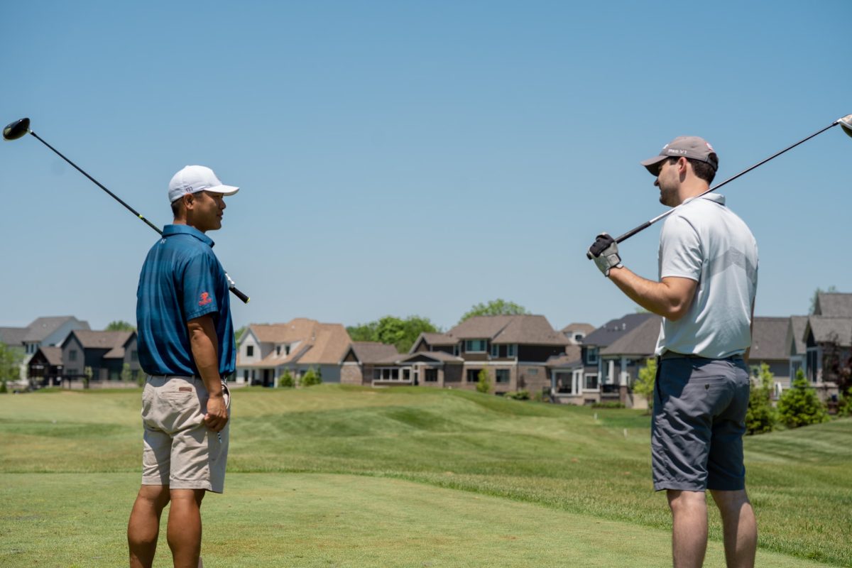 Two people looking at each other while holding their golf clubs over their shoulders