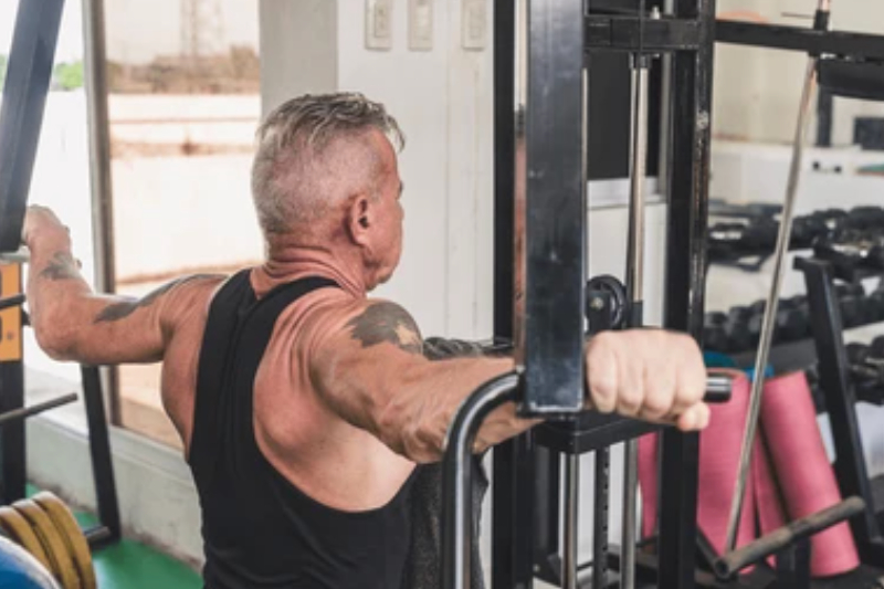 Older gentleman performing a reverse fly on a fly machine in a gym.