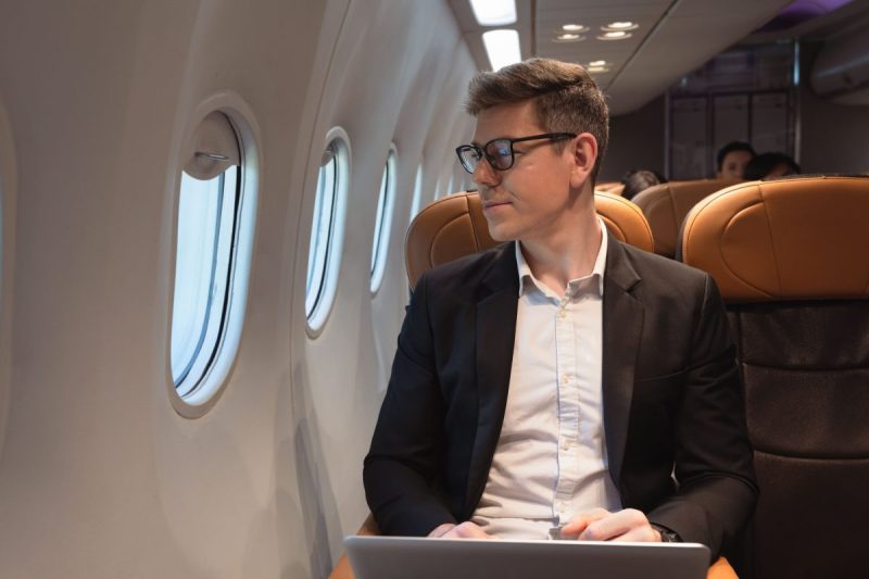 Hombre sentado en un avión mirando por la ventana con una computadora portátil en su regazo.