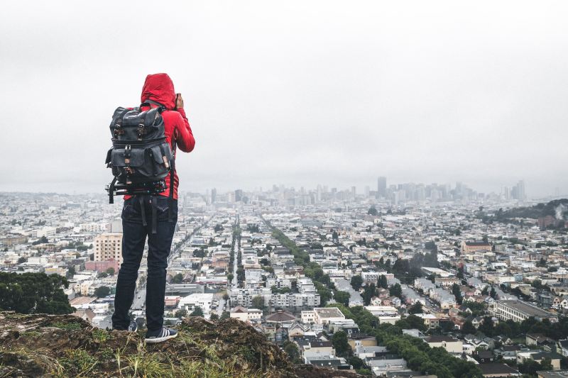 Hiker in a red hoodie taking photos overlooking San Francisco, California.