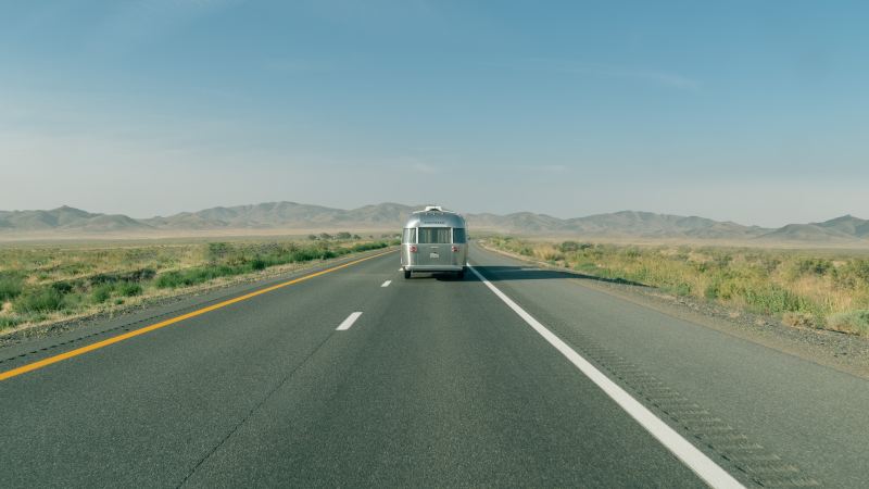 Long shot of the rear of an Airstream travel trailer being towed down a wide-open desert road.