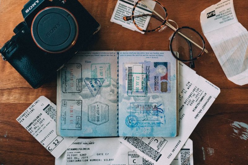 An open passport on a table with a pair of glasses and a camera around it.