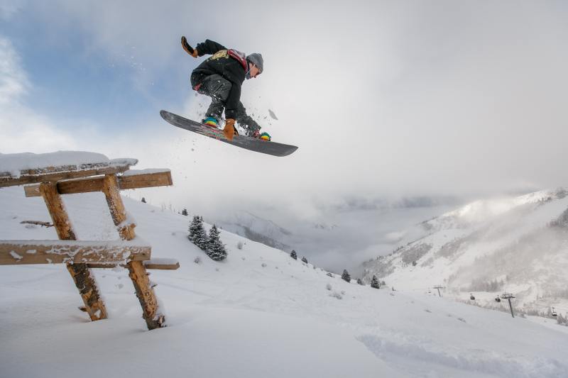 A man jumps off a picnic table on a snowboard