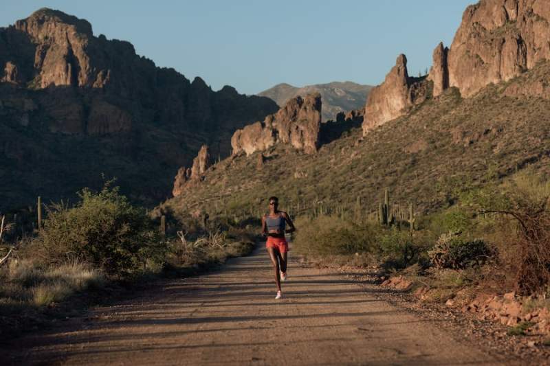 A runner on a dusty track with scrubland and rocky outcrops in the background.