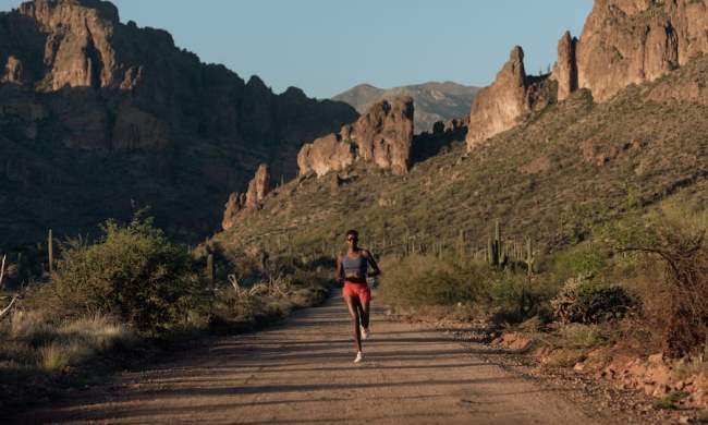 A runner on a dusty track with scrubland and rocky outcrops in the background.