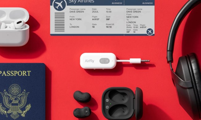 AirFly device, headphones, passport, airpods, and plane ticket spread out on red table.
