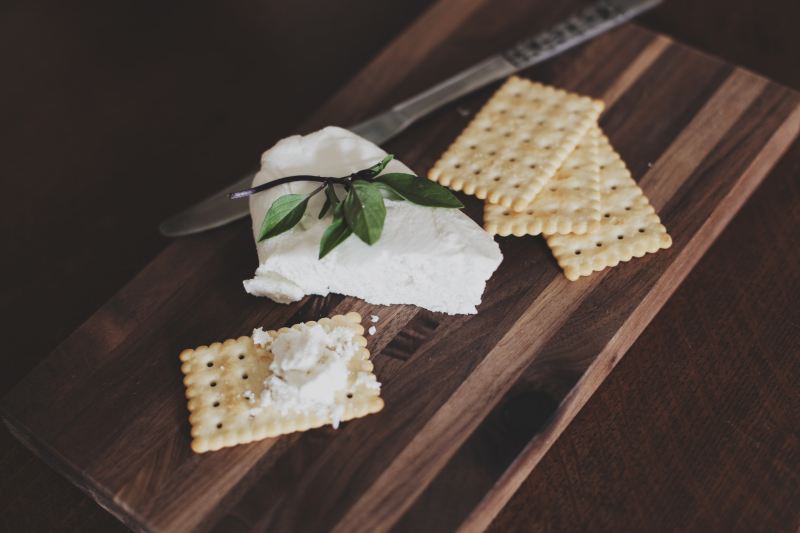 Cream cheese and crackers on a wooden cutting board.