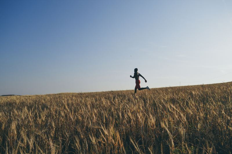 A man runs across a field of hay in the dwindling sun