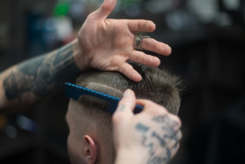 a man getting a haircut from tattooed barber