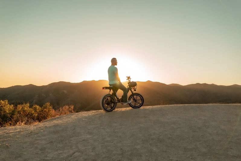 Man sitting atop an ebike with mountains and the setting sun in the background.